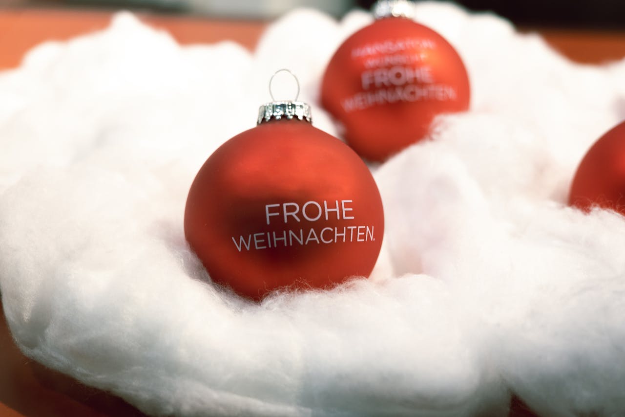 Close-up of a red Christmas ornament with 'Frohe Weihnachten' on fluffy snow-like material.